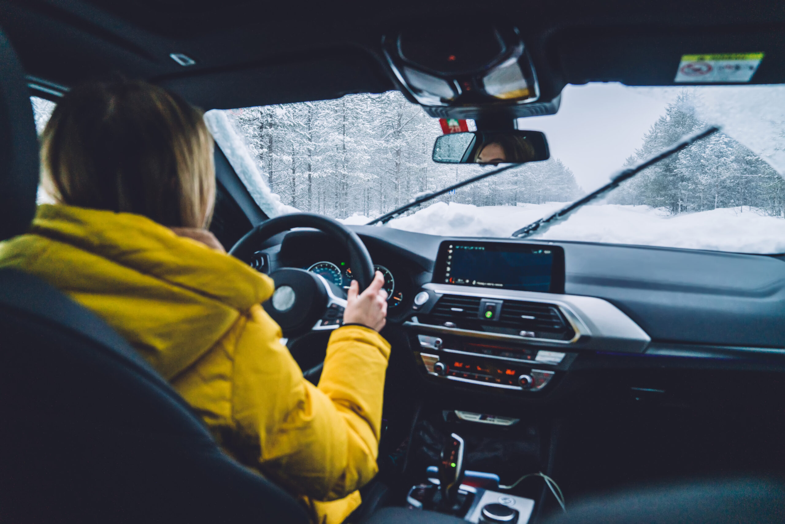 Woman in yellow jacket safely driving her car during snowy conditions