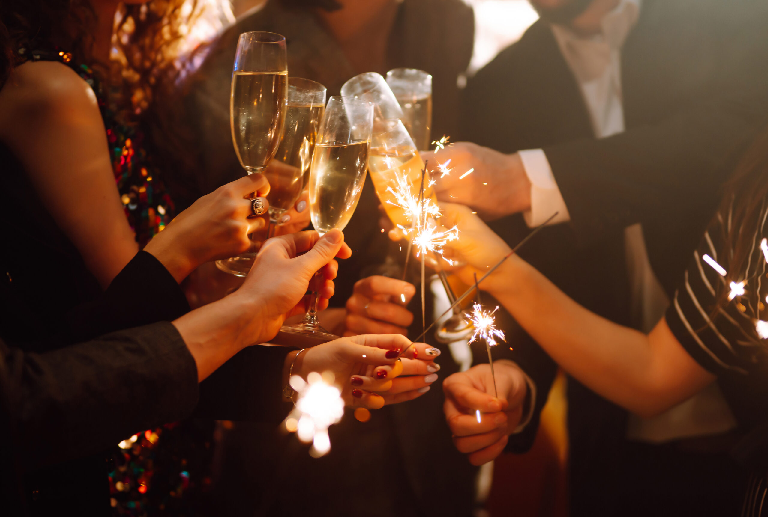 Group of happy people holding sparklers and clinking glasses of champagne at a holiday party