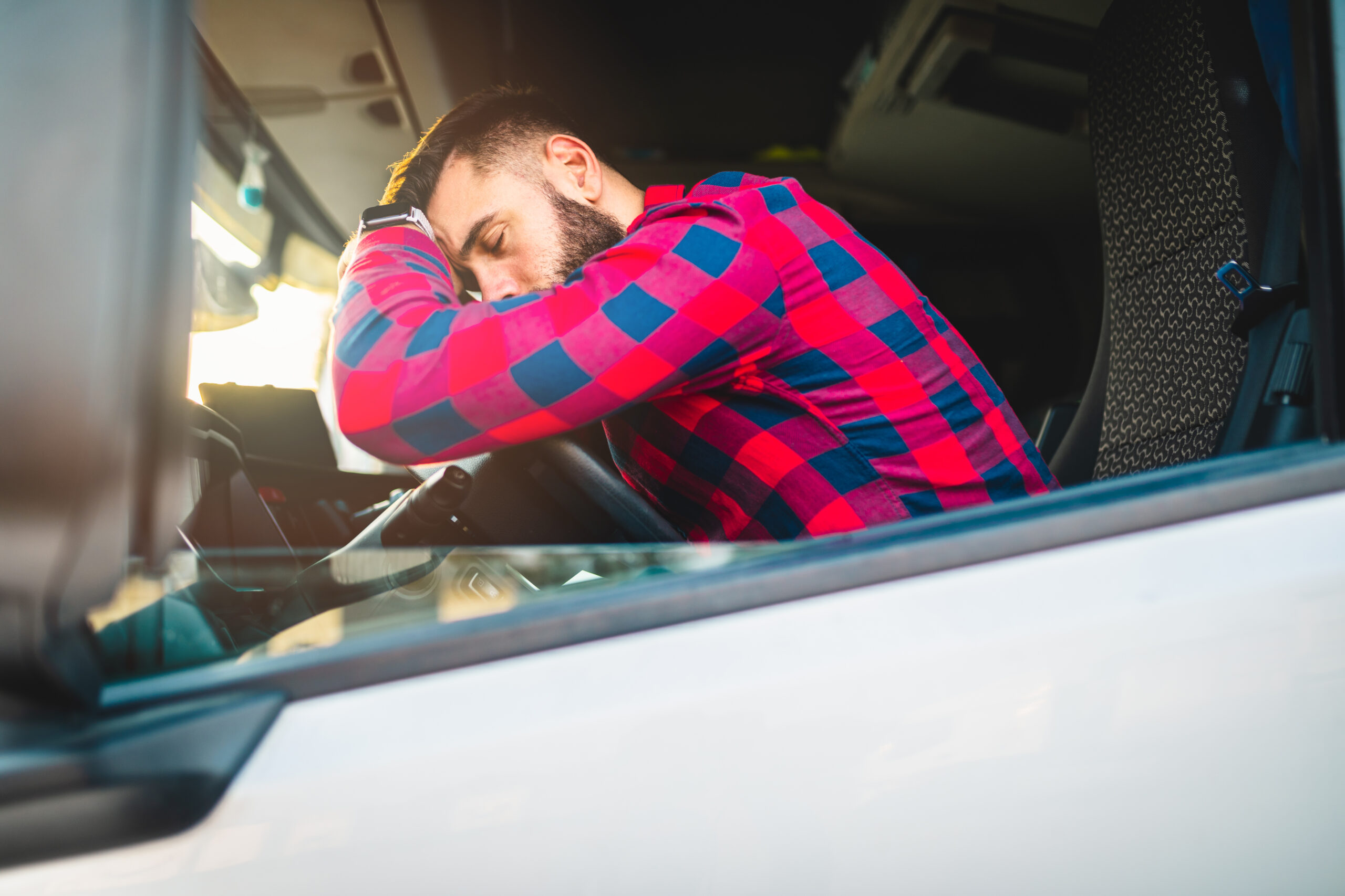 Overworked truck driver, asleep on the steering wheel of his semi-truck