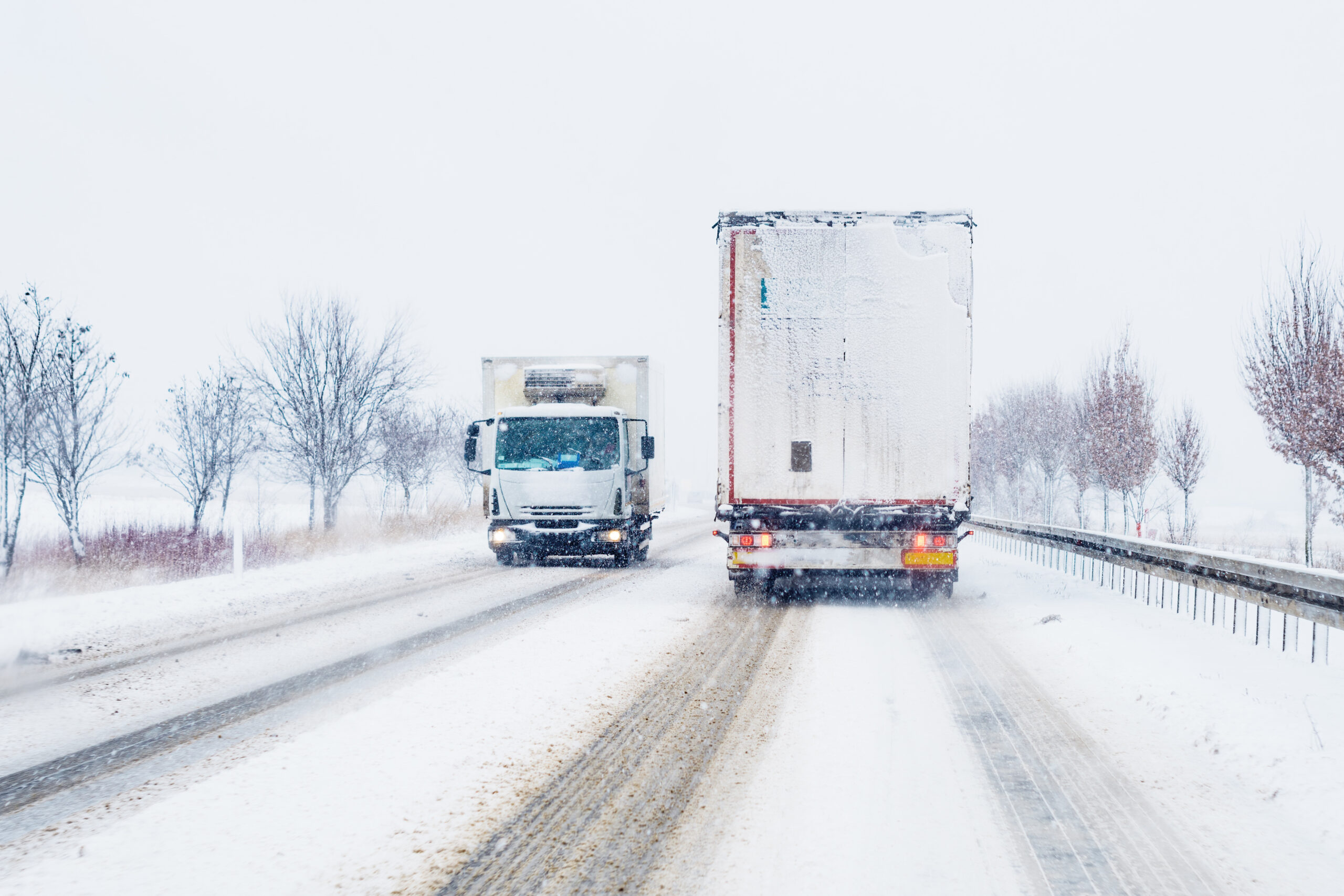 Two large trucks, driving during a blizzard with snow and ice