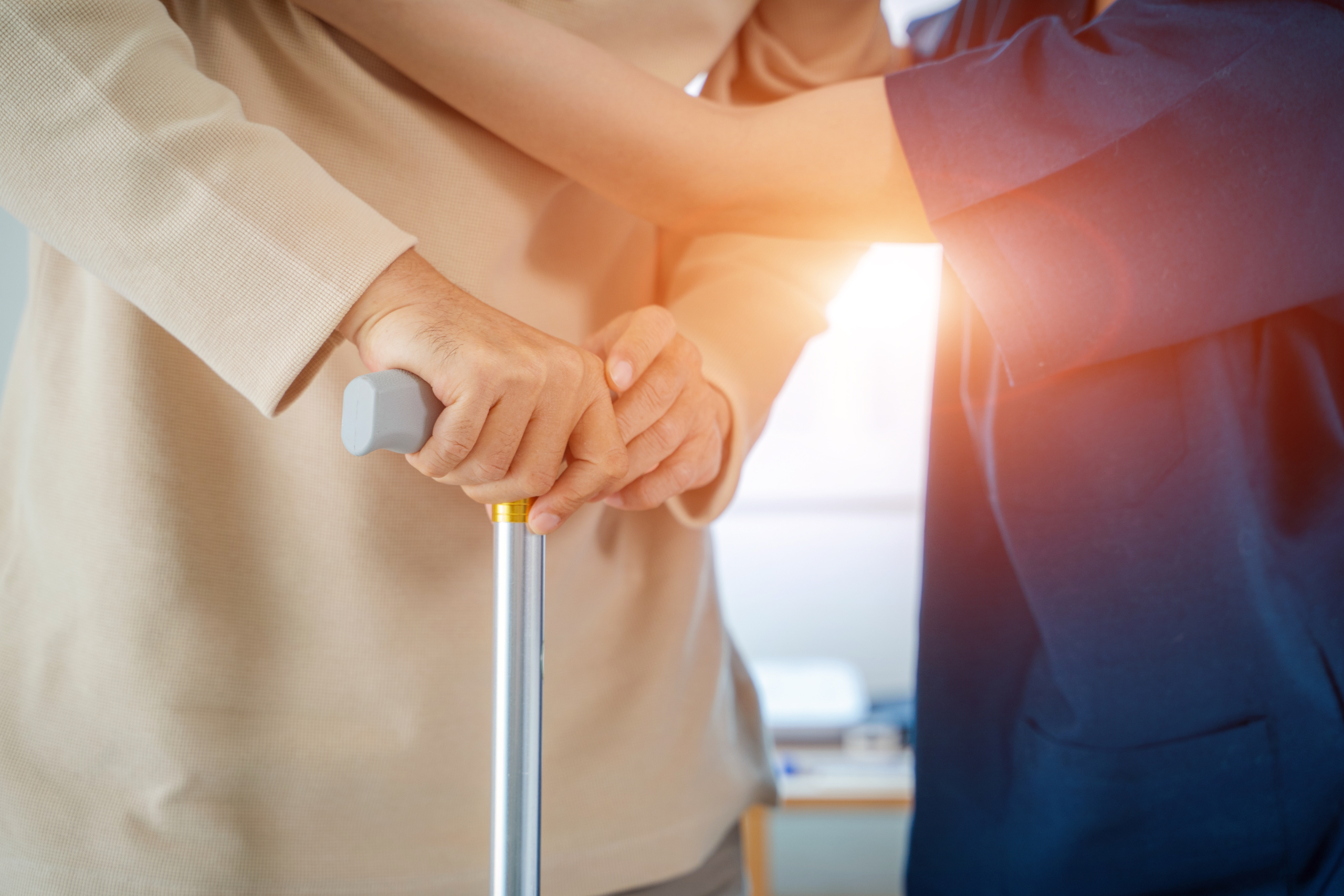 Close-up of a supportive caregiver's hands gently guiding an elderly person's hands on a walking cane, symbolizing the trust and care provided to seniors, relevant to articles on being knowledgeable and attentive to a loved one's needs.