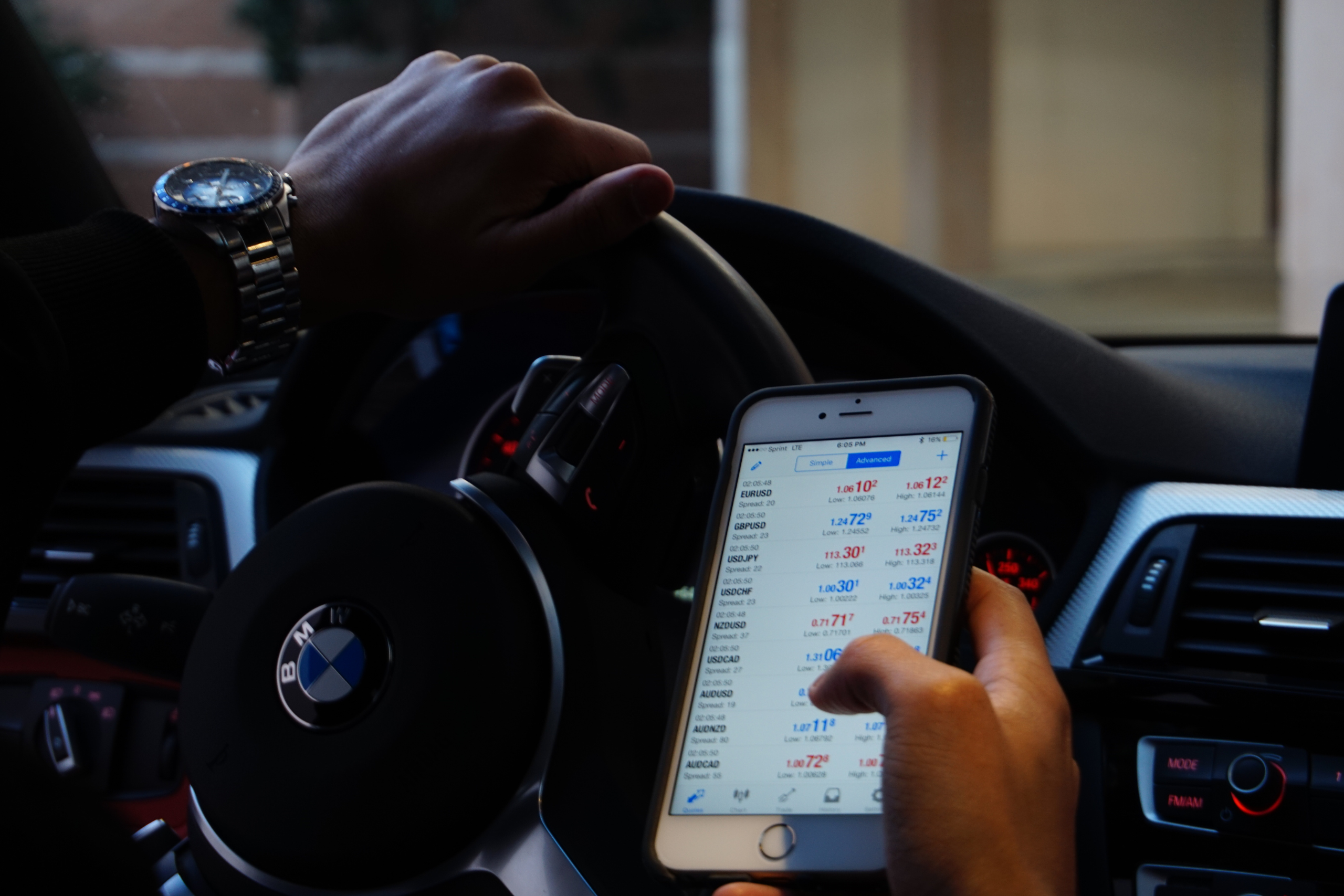Driver in a BMW vehicle looking at a smartphone with financial information on screen, illustrating potential distracted driving.