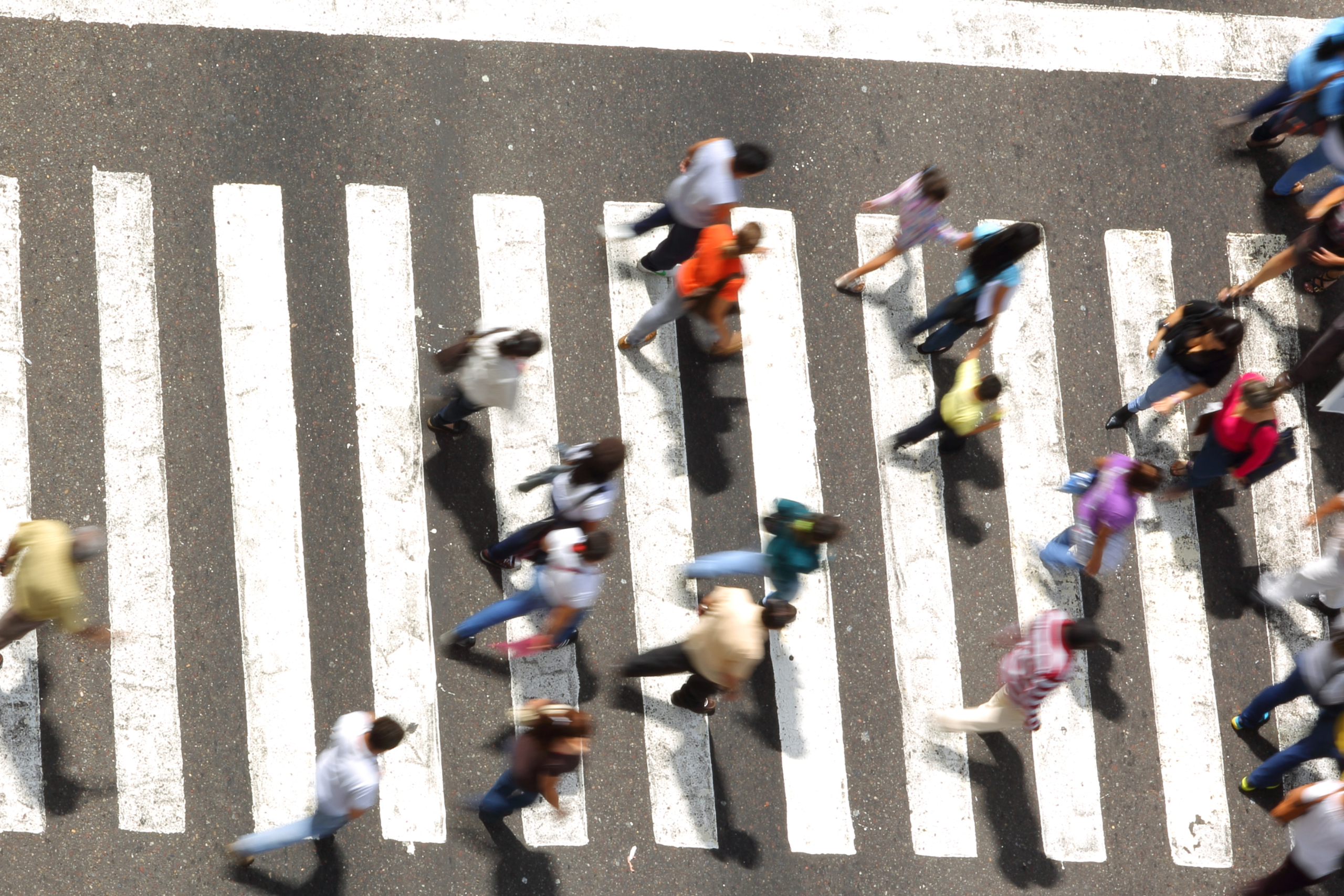 Pedestrians crossing a street at a zebra crossing, emphasizing the importance of pedestrian safety during National Traffic Awareness Month.