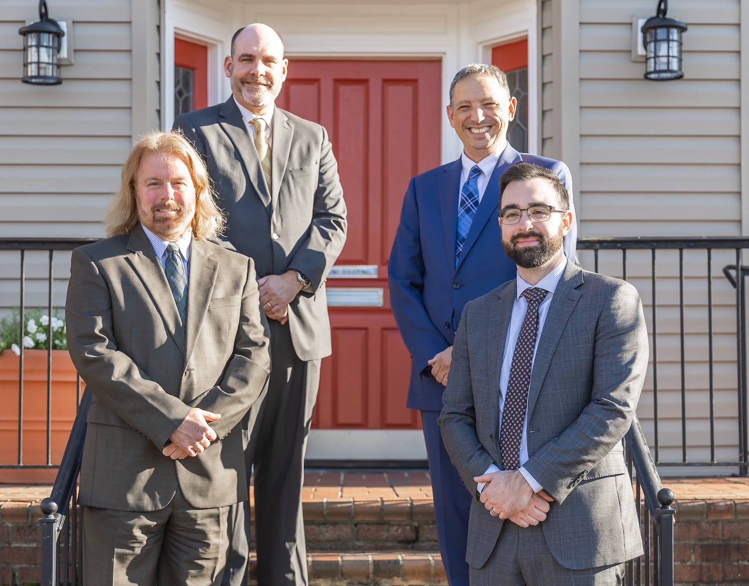 Four professionals in suits standing in front of a red door and a traditional building, posing for a group photo.