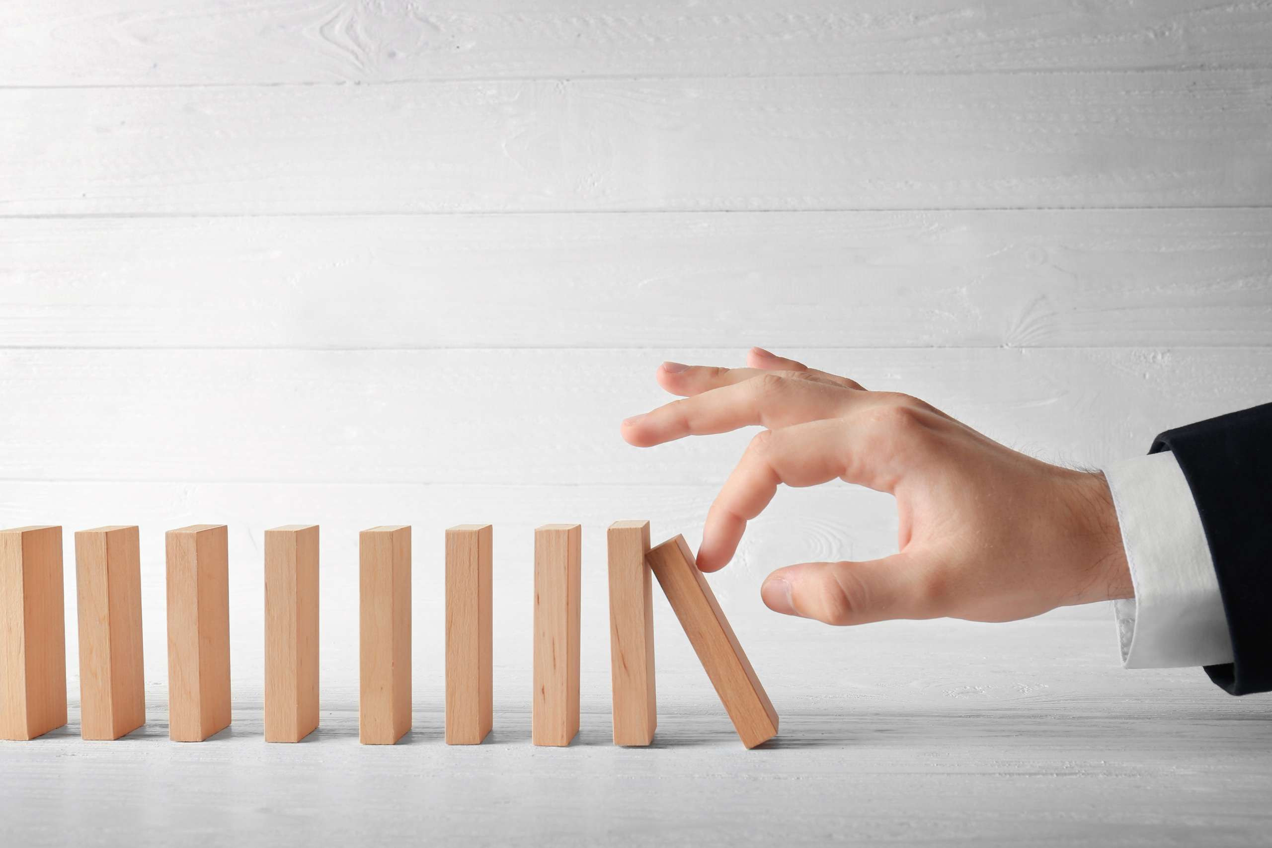 Hand in a suit knocking over wooden blocks like dominoes, symbolizing a chain reaction in a nursing home.