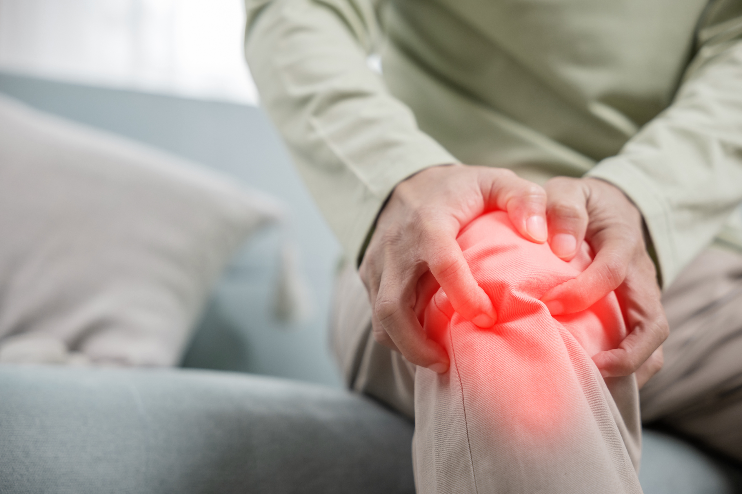 Person in a nursing home clutching their painful knee, highlighted in red, while sitting on a couch.