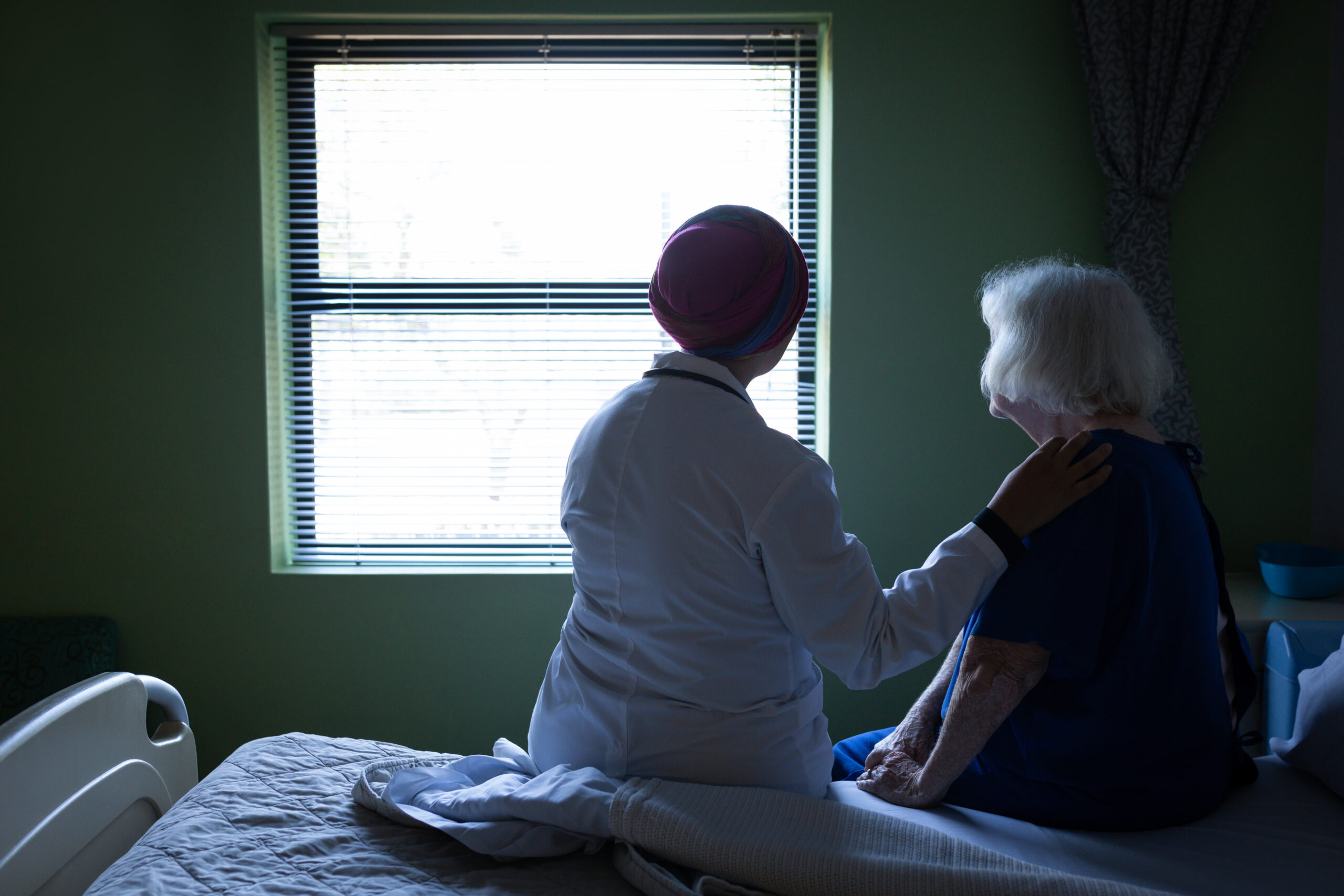 Nurse comforting an elderly woman by a window, symbolizing support and the importance of knowledge in nursing home advocacy.