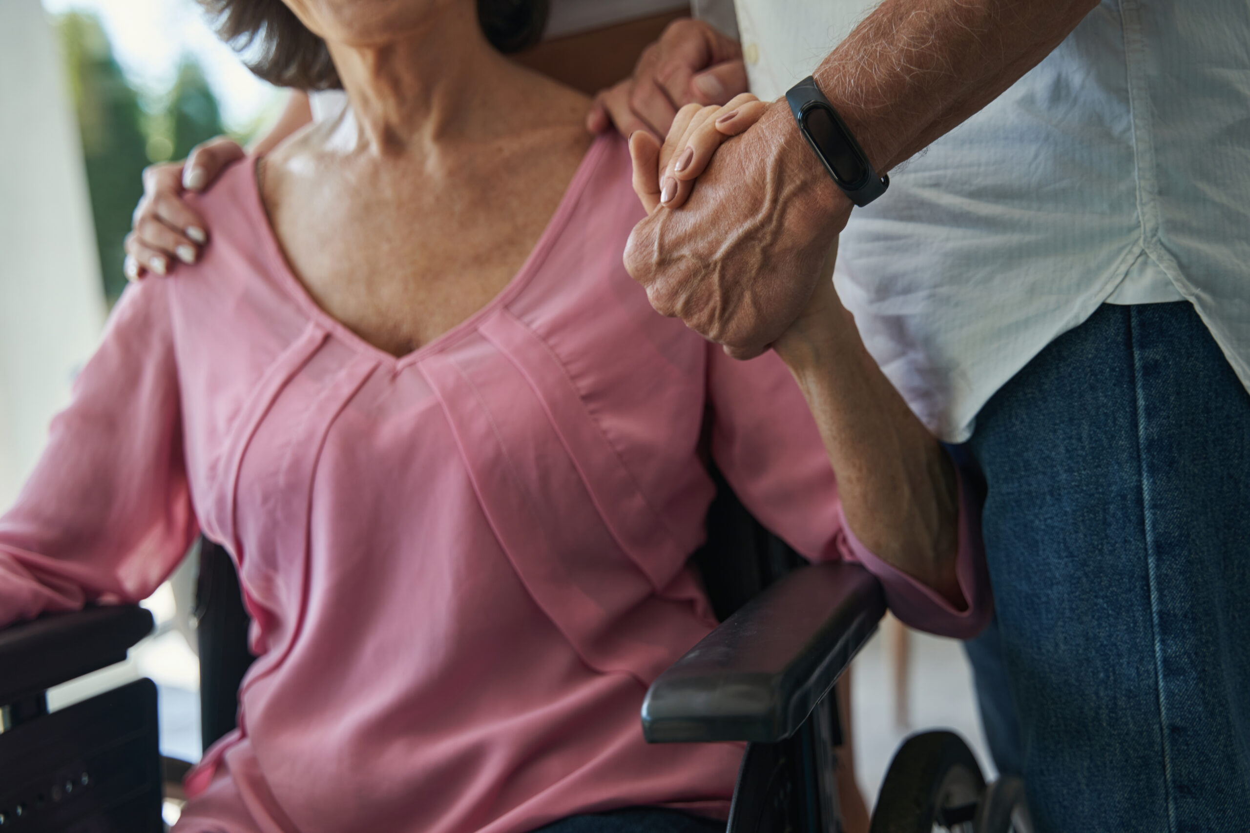 Close-up of a caregiver holding an elderly woman's hand while she sits in a wheelchair, emphasizing the importance of movement in nursing home care.