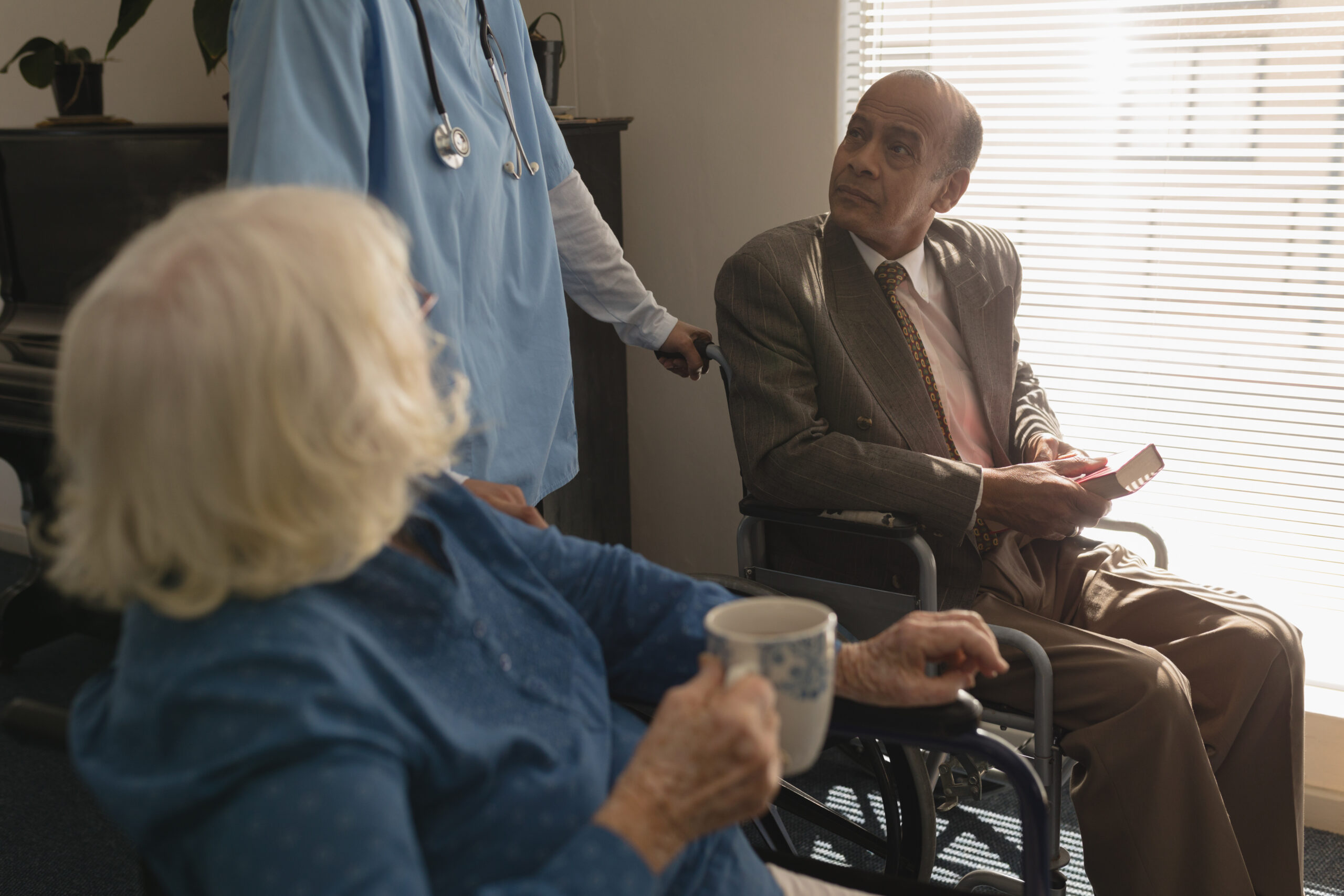 Elderly man in a wheelchair and woman with a cup, both interacting with a nurse, highlighting potential signs of caregiver negligence.