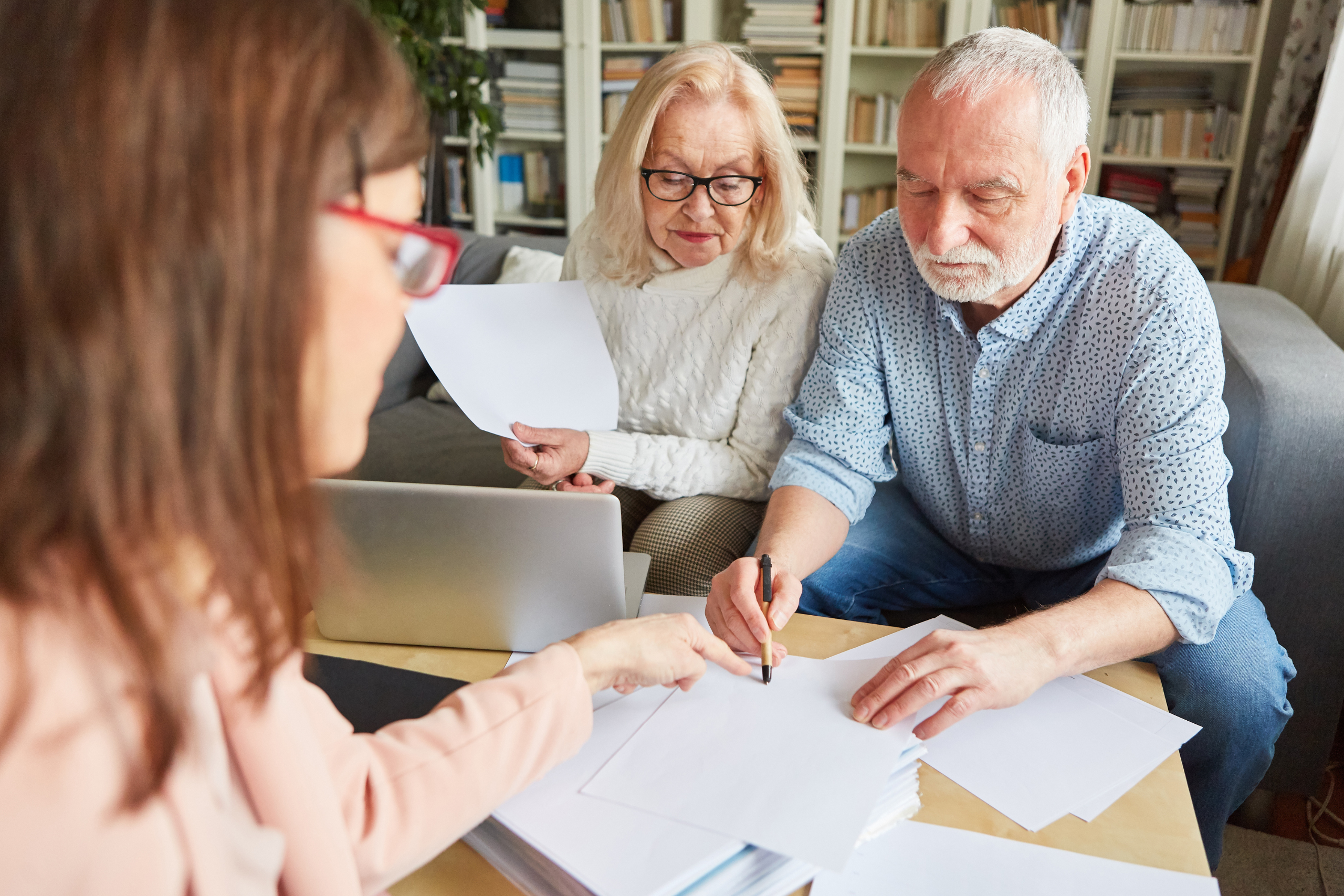 Elderly couple reviewing and signing documents with a female advisor in an office, emphasizing legal or financial consultation.