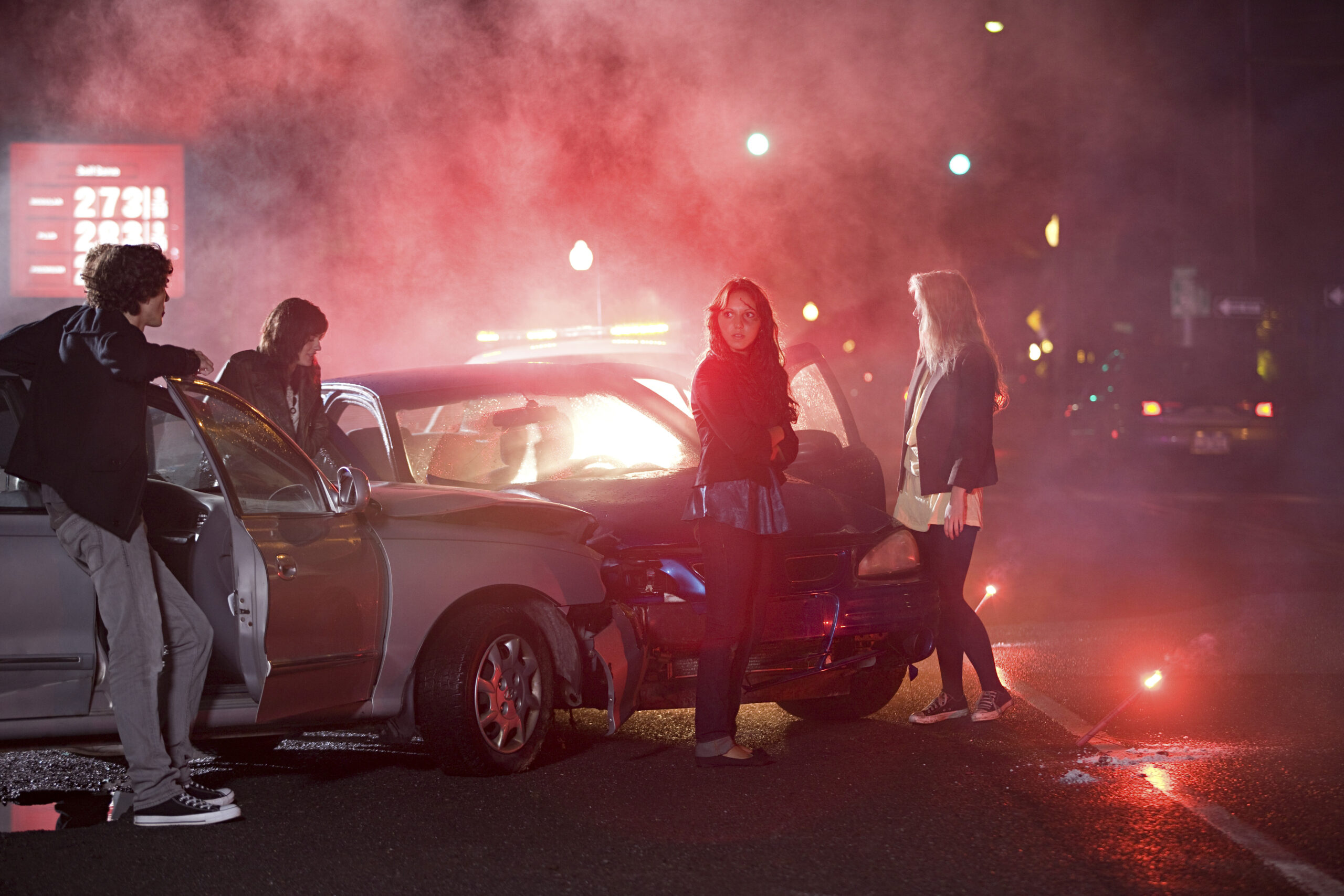 A group of people gathered around a car at a foggy nighttime roadside