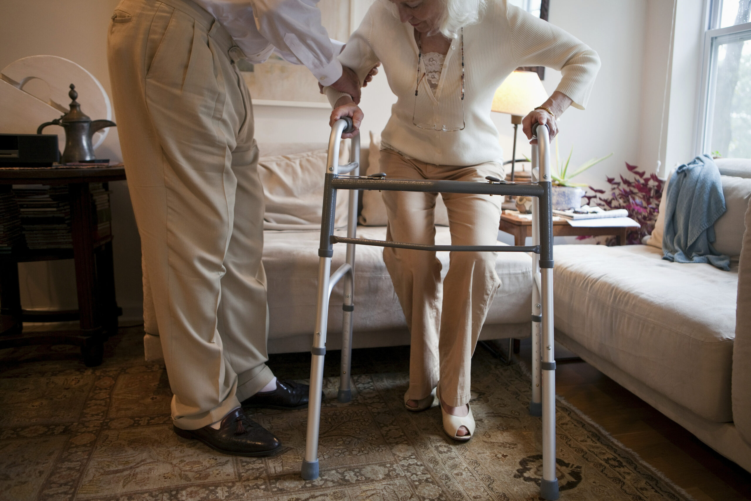 Elderly woman using a walker with assistance, highlighting the importance of mobility aids and caregiver support for safe movement.