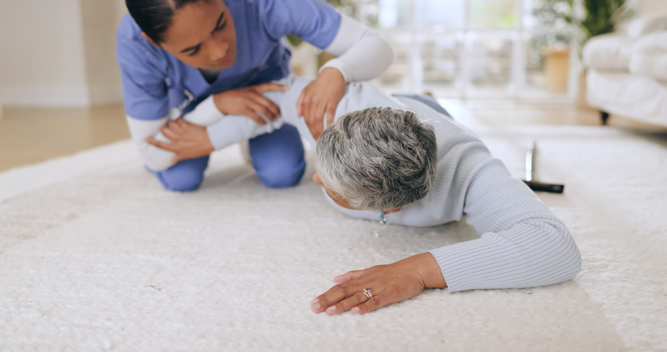 Nurse assisting an elderly woman who has fallen on a carpeted floor, highlighting the importance of immediate care and fall prevention strategies.