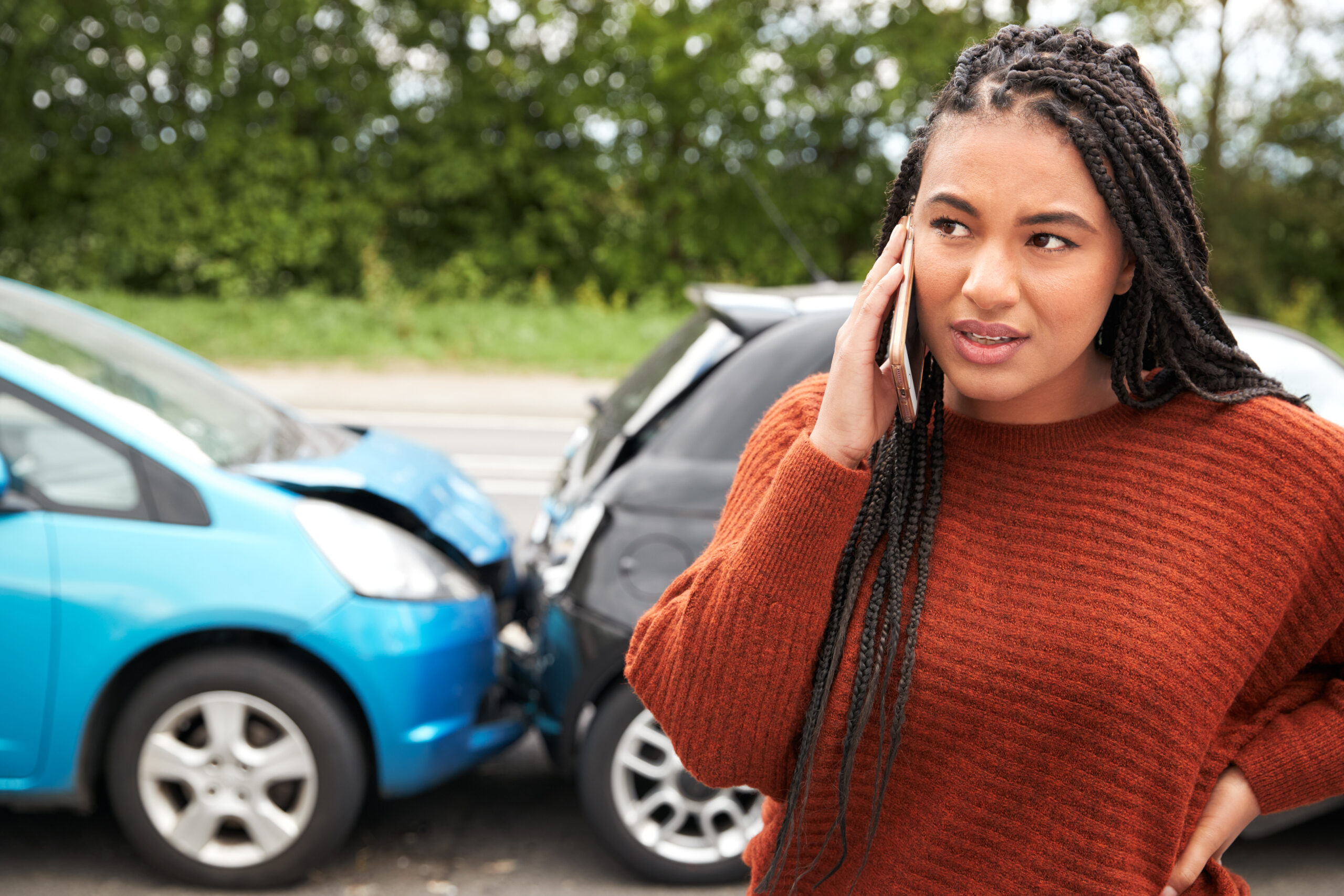 Concerned woman on the phone near two cars involved in a rear-end collision, highlighting the immediate aftermath of an accident.