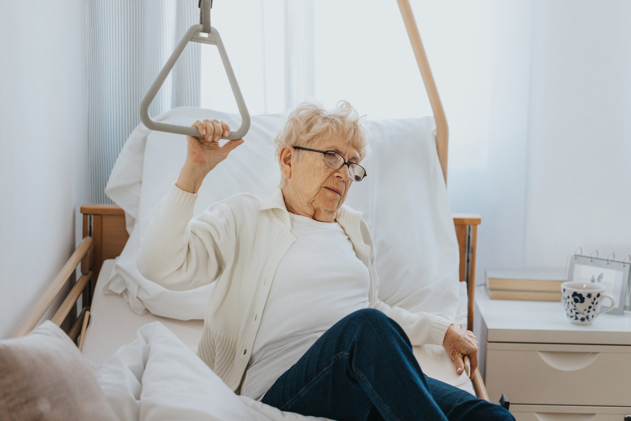 Elderly woman using a bed assist rail to sit up, illustrating mobility aids and their role in maintaining independence and safety.