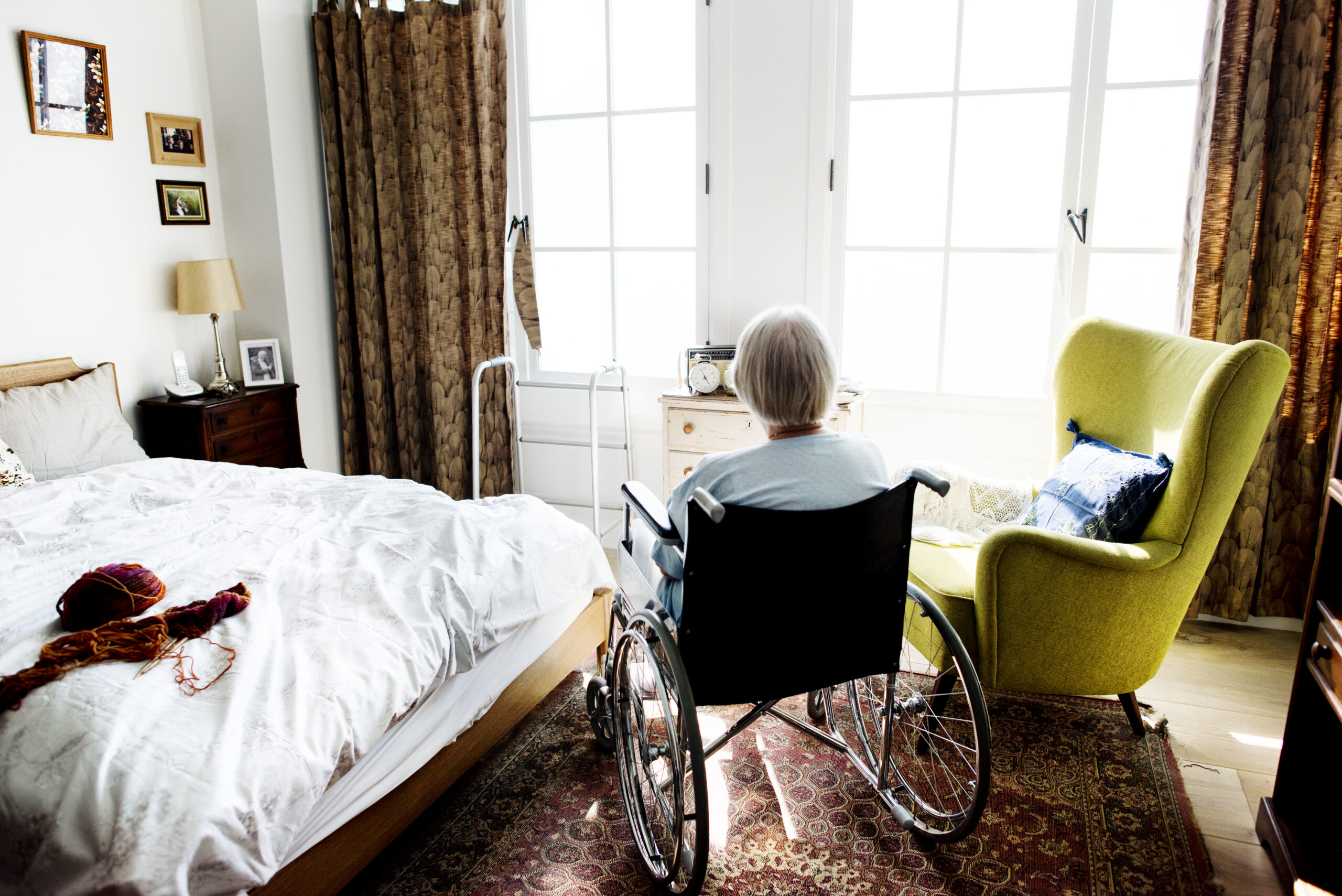 Elderly woman in a wheelchair sitting in a cozy bedroom, symbolizing the importance of accessibility and comfortable living environments.