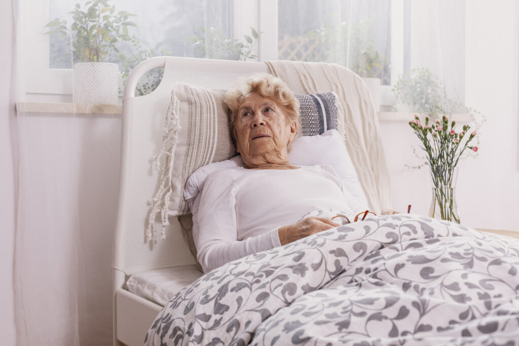 Elderly woman lying in bed looking distressed; Williams DeLoatche highlights importance of documenting nursing home neglect.