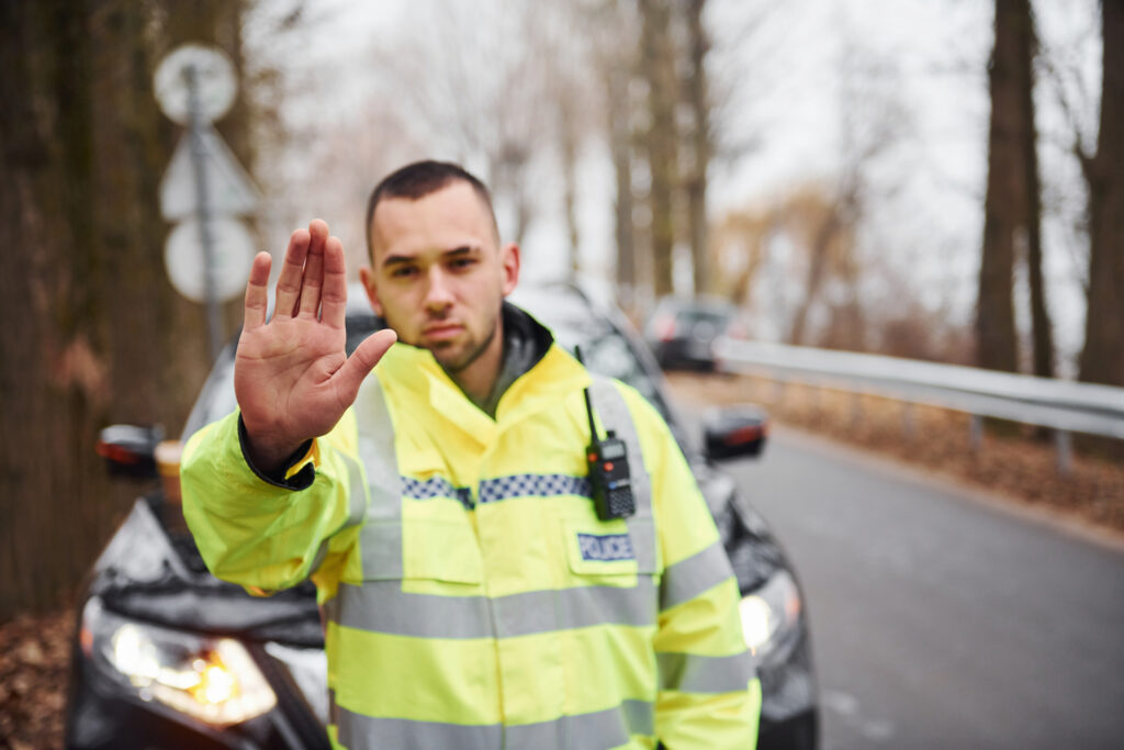 Police officer in high-visibility jacket signaling stop with raised hand during roadside traffic control
