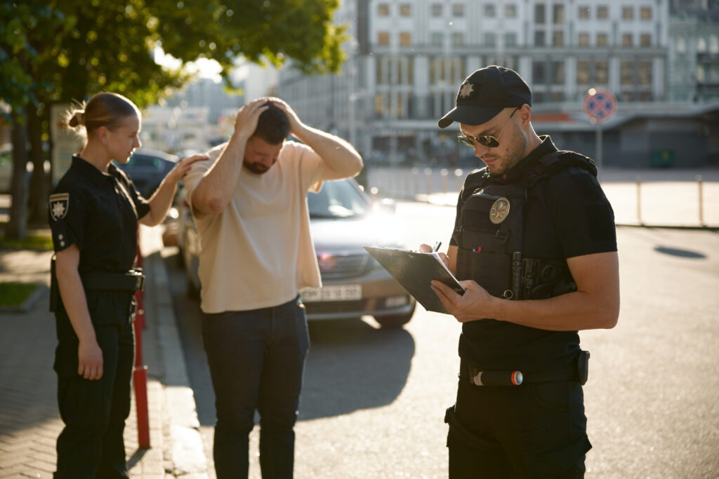 Male driver holding head in frustration as police officers issue a traffic citation on city street
