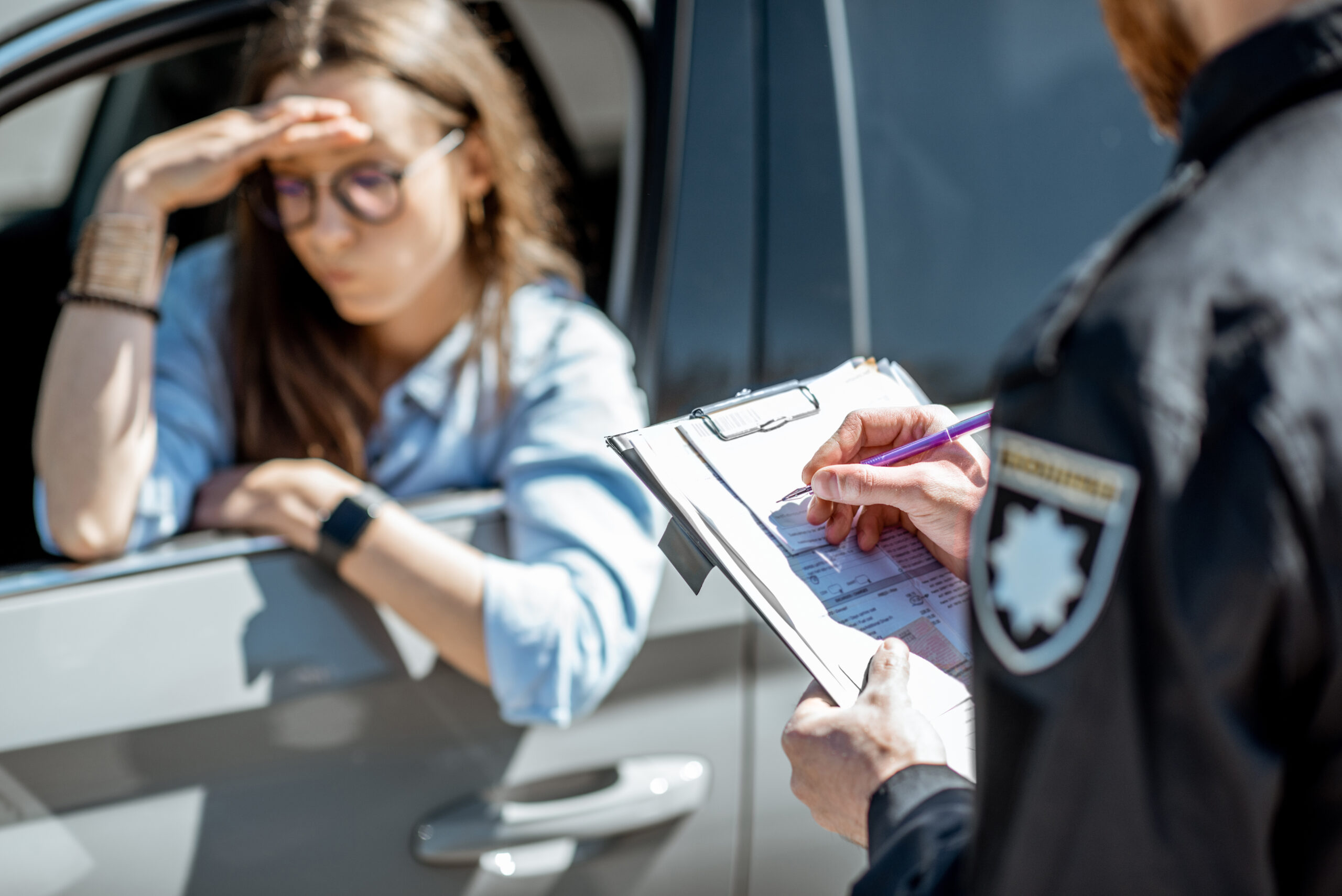 Female driver looking stressed as police officer writes a speeding ticket outside her car window