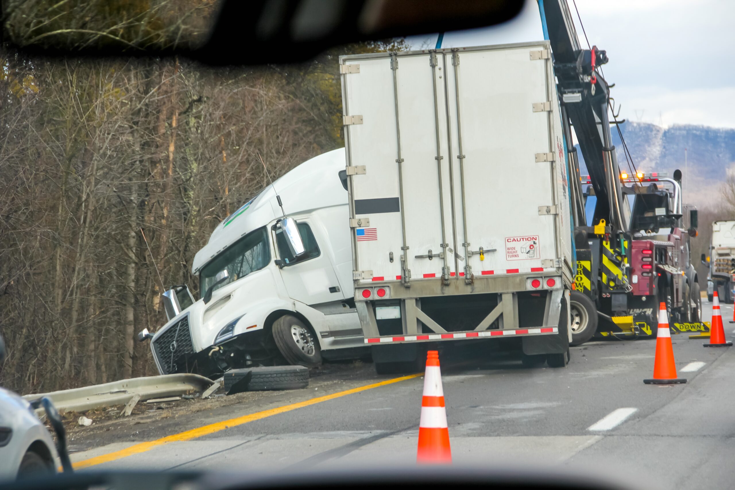 Semi-truck crash being towed after highway accident near wooded area