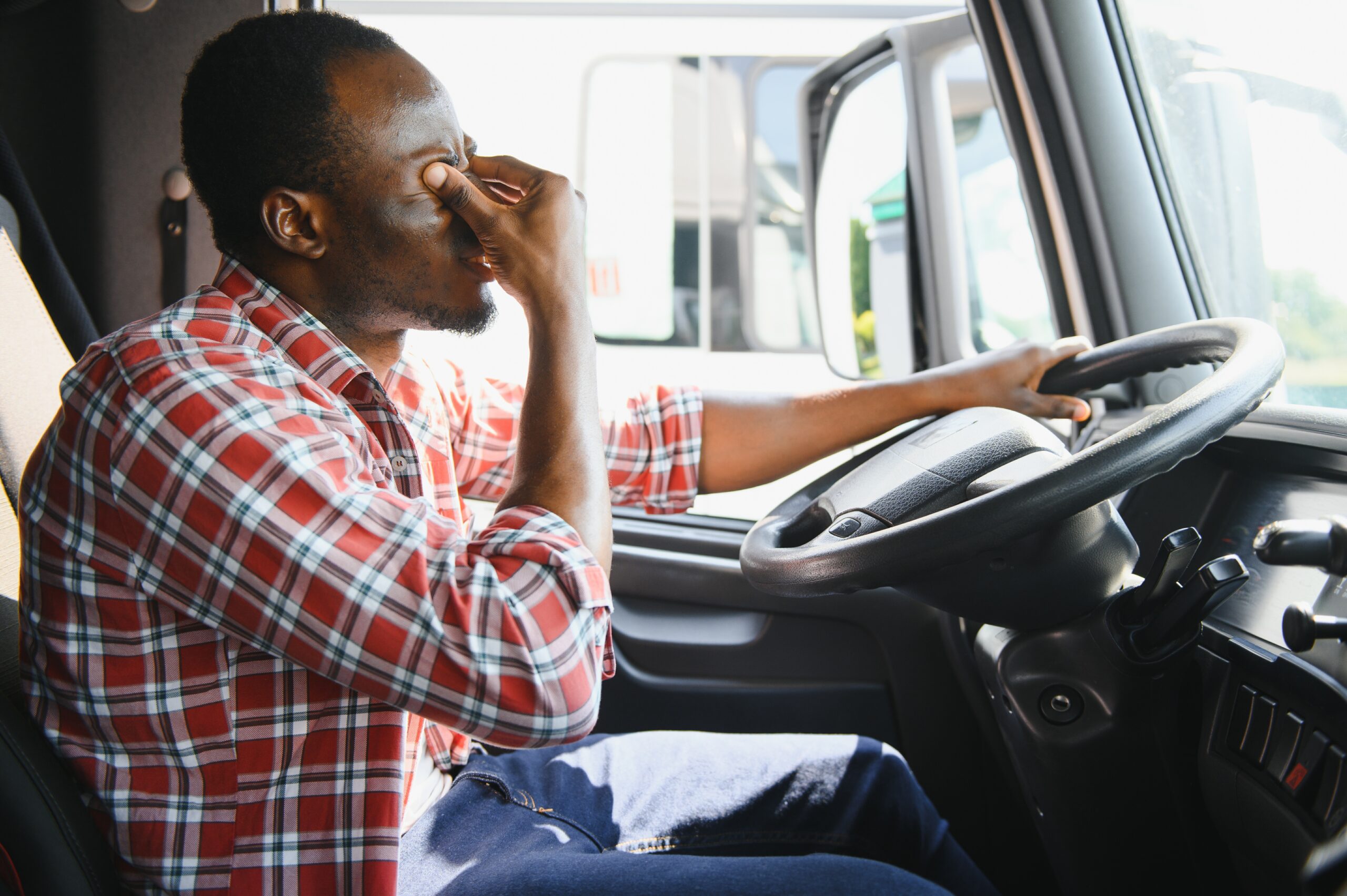 Tired truck driver rubs eyes while sitting in cab, emphasizing fatigue as a cause of trucking accidents