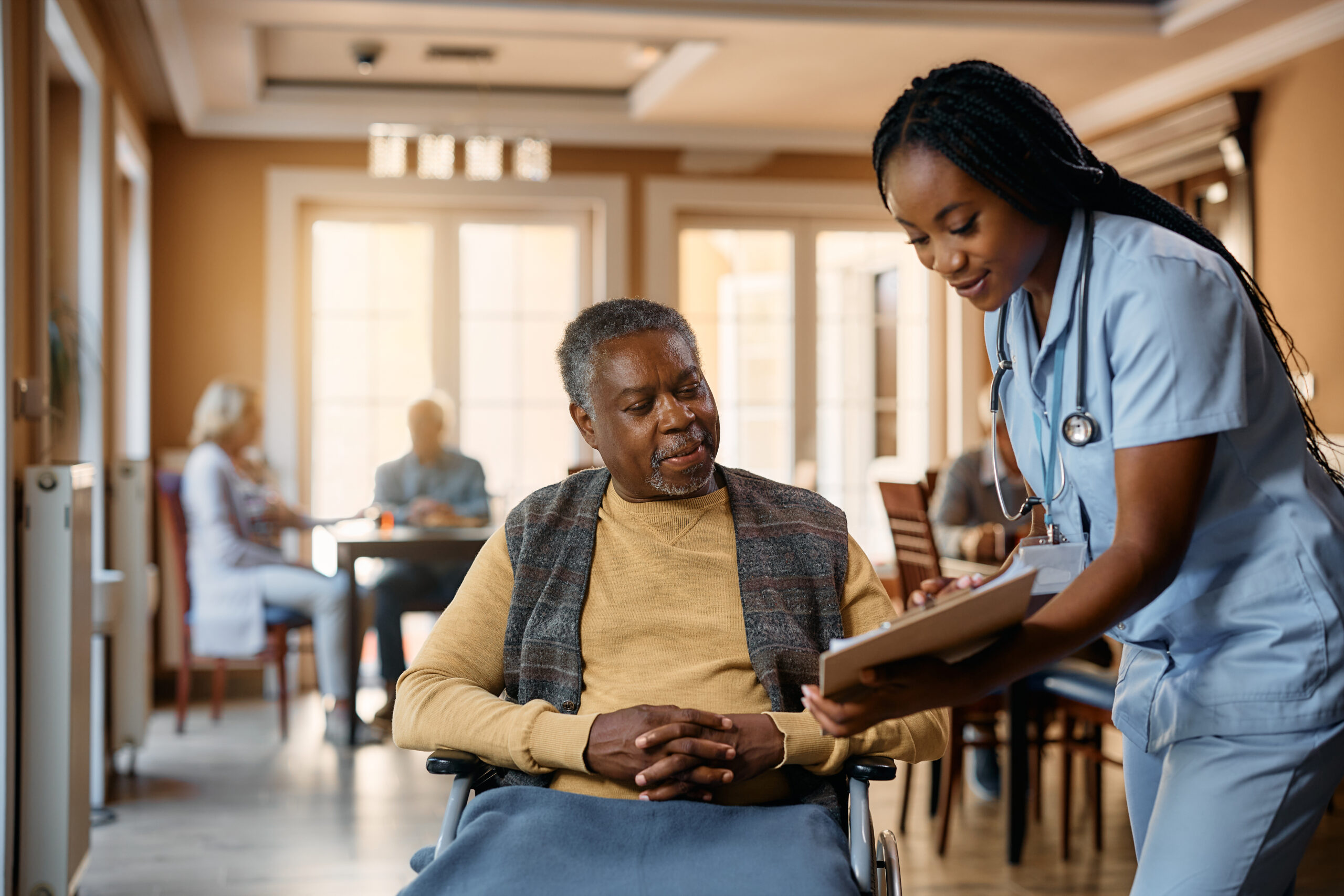 Female nurse at a nursing home goes over an elderly man in a wheelchair’s medical chart