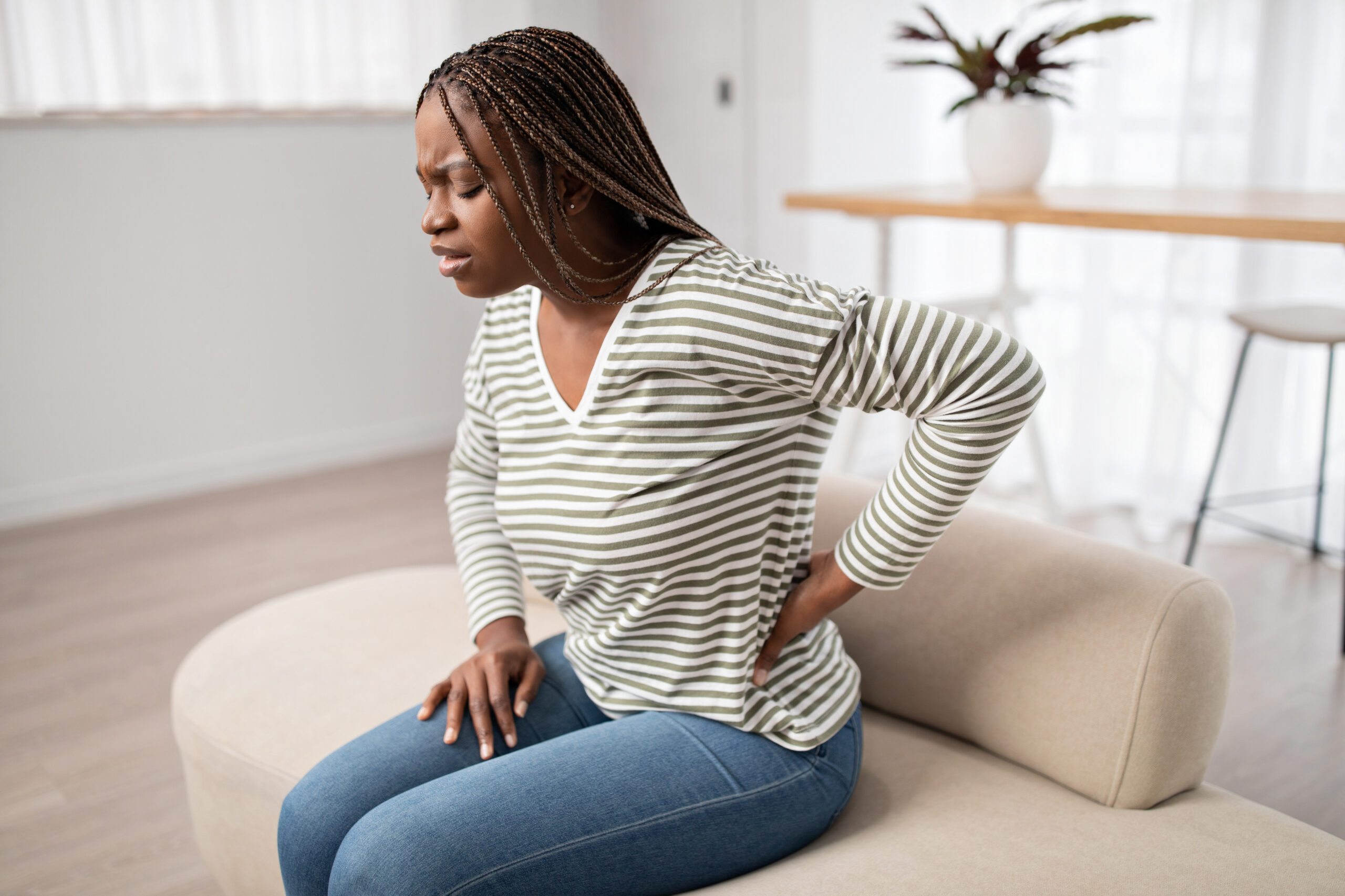 Woman sitting on a couch holding her lower back in pain, illustrating the physical impact of injuries and the importance of proper claims.