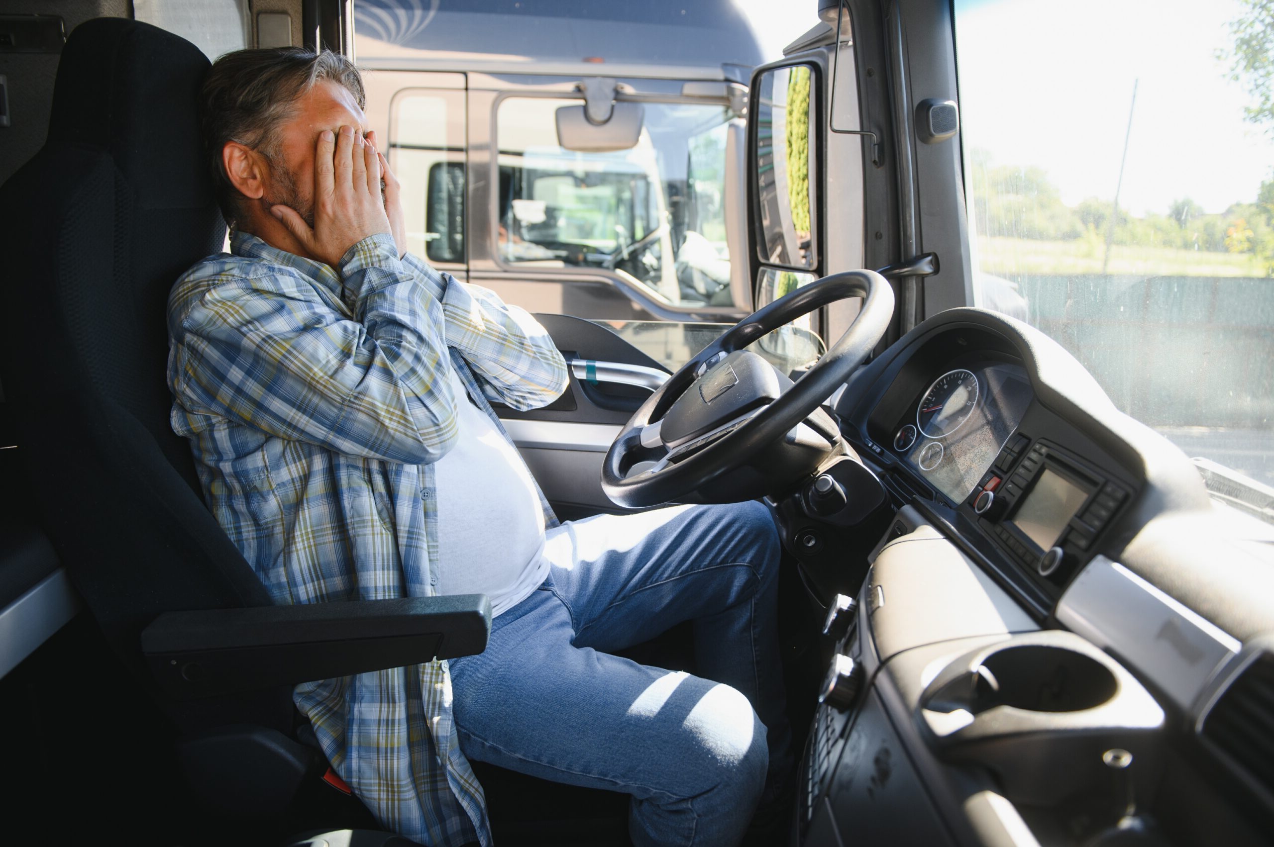 Stressed truck driver sitting in cab with hands covering face