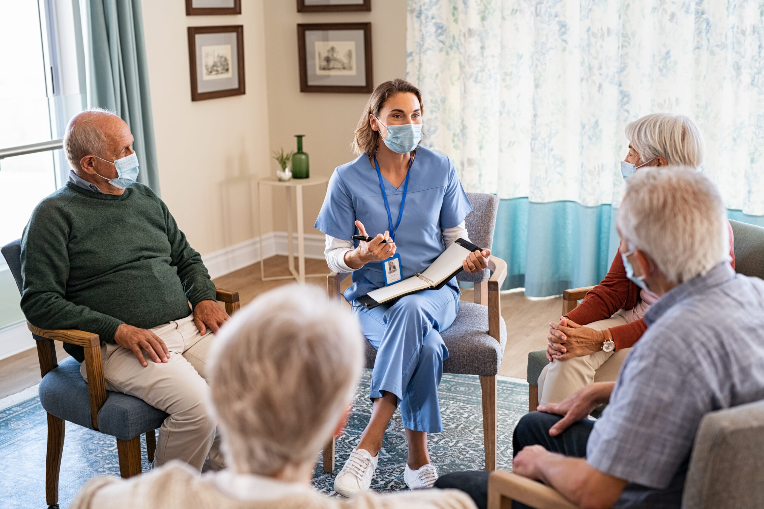 A healthcare worker in blue scrubs leading a discussion with a group of elderly residents in a nursing home, focusing on care planning. 