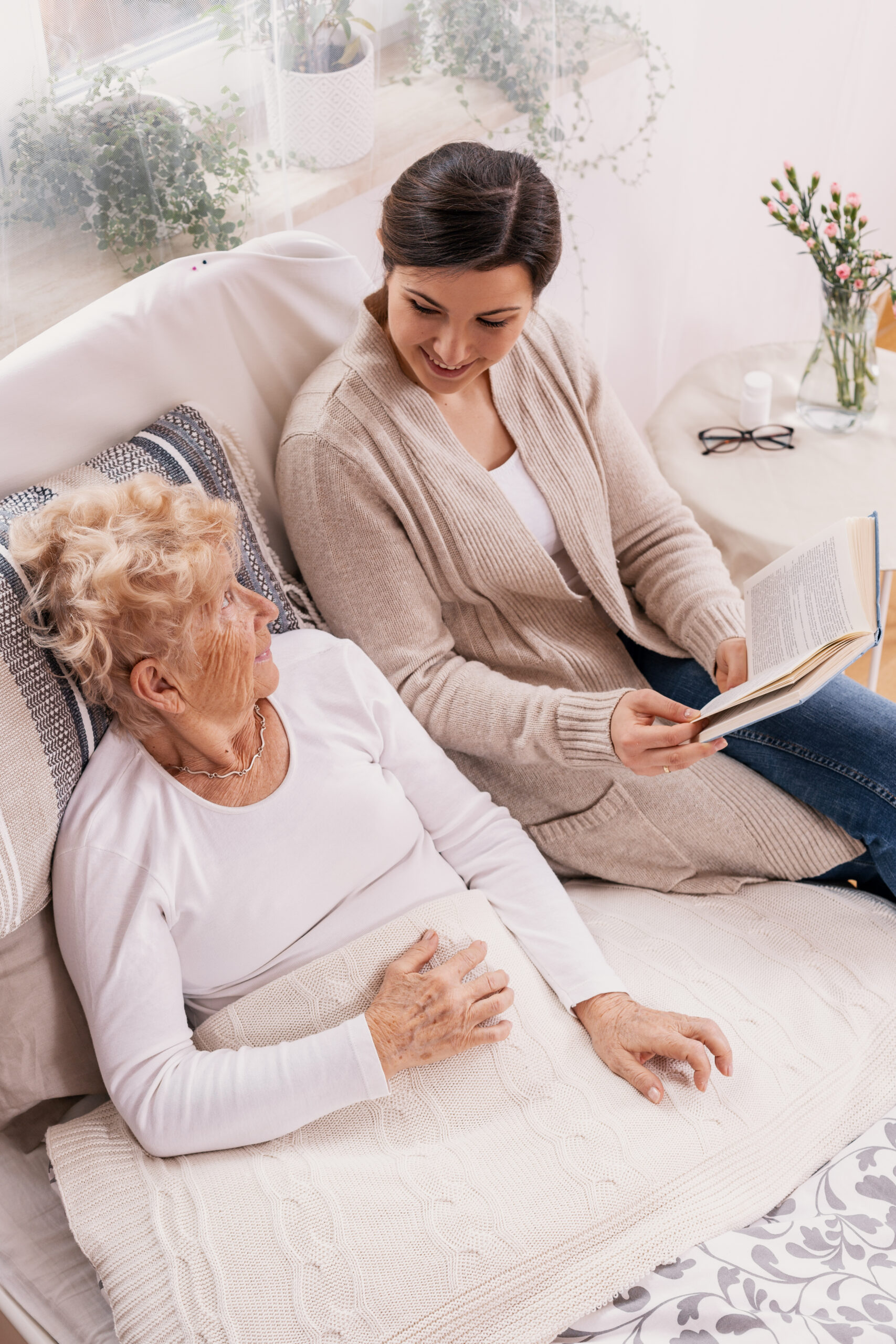 Concerned woman reading to elderly mother in bed; Williams DeLoatche advises families to document signs of nursing home neglect. 
