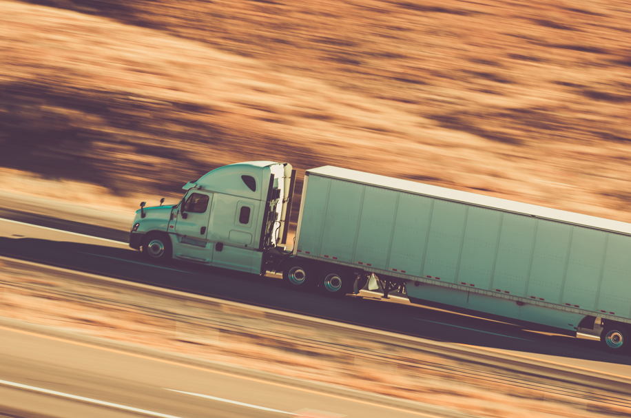 Semi-truck driving on highway through desert landscape at high speed