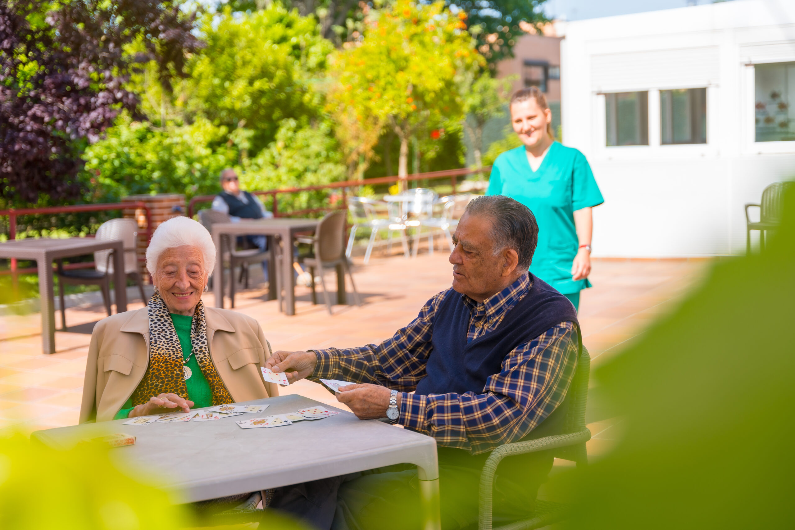 Lora – Williams DeLoatche, P.C. Smiling seniors playing cards at nursing home under staff supervision; Williams DeLoatche advocates for elder care rights.