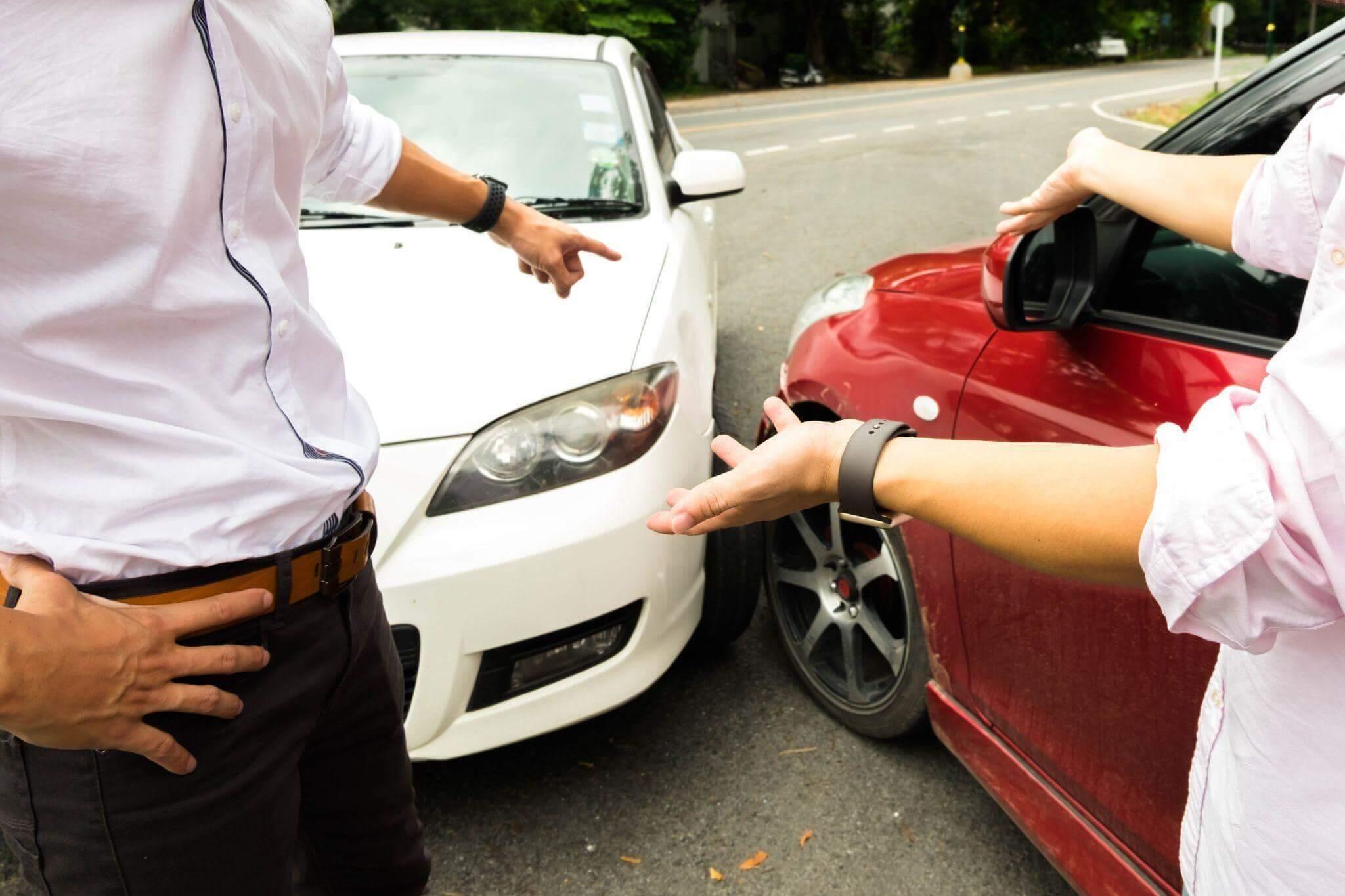 a man and a woman standing next to a red car that collided with a white sedan in an open road